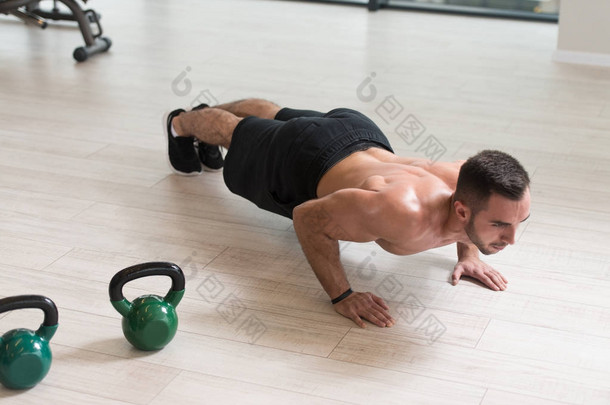 健美男子运动员在健身房用水壶铃做仰卧起坐锻炼- -水壶铃运动