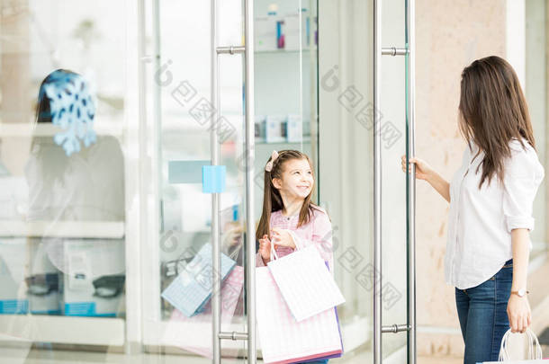 女儿拿着五颜六色的购物袋, 走进商店与母亲 