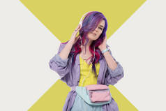 时尚的年轻妇女与彩色头发在紫色的战壕大衣听音乐与耳机