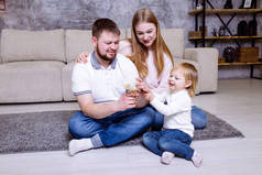 小女孩, 她的父亲和母亲正在家里玩小鸡, 微笑着。金发碧眼的小女孩和她的家人坐在家里的地毯附近的沙发上。家庭复活节庆祝