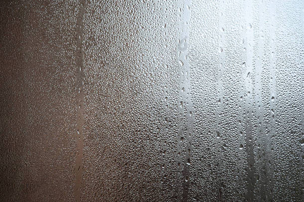 窗户玻璃表面的照片, 上面覆盖着各种各样大小的水滴。玻璃上致密凝结层的背景纹理