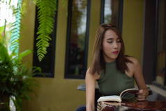 一个美丽的年轻女子在房子附近的咖啡馆的肖像。心情好。一个美丽的年轻女子的肖像读一本书放松和舒适