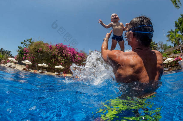 快乐活泼的家庭年轻父亲与活跃婴儿潜水在游泳池与乐趣跳跃有趣的照片 . 