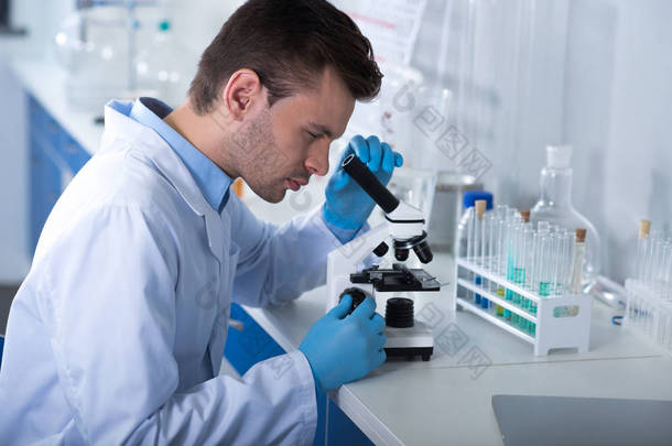 微生物学研究。年轻英俊<strong>认真</strong>的探险家坐在实验室进行研究和使用显微镜.