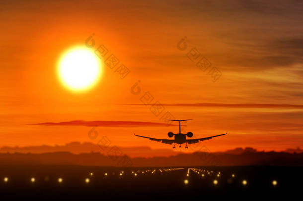 飞机剪影在日落时降落在机场。太阳, 私人喷气飞机的形状和闪烁的跑道灯.