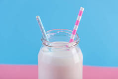 在柔和的背景下, 用两根吸管的鲜牛奶玻璃瓶。多彩简约。健康乳制品与钙的概念