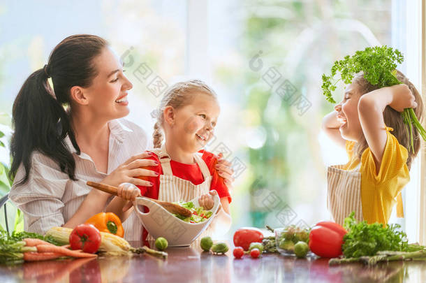 健康的食物在家里。幸福的家庭在厨房里。母亲和孩子的女儿们正在准备蔬菜。.