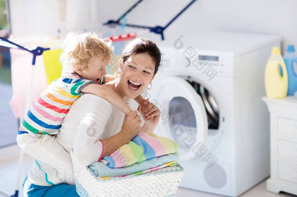 母亲和孩子在洗衣房里用洗衣机或滚筒烘干机。家庭琐事。现代家庭设备和洗涤洗涤剂在白色阳光的家。烘干机架<strong>清洗</strong>洗衣服. 