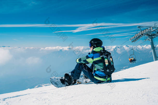 年轻的滑雪板坐在山顶上欣赏着云层的景色。坐在云层之上。美丽的冬天自然在山里.