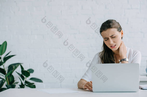 年轻的女商人在使用膝上型电脑时患有颈部疼痛 