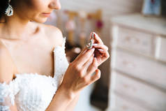 在婚纱礼服上的一个年轻女孩的裁剪框架特写检查耳环。新娘的指甲, 婚礼的装饰品。新娘费的概念, 上午.