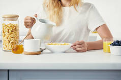 妇女的部分看法与牛奶罐坐在桌与碗玉米片和杯子果汁在家庭早餐