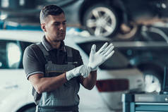汽车修理工穿着白色手套在车库。英俊严肃的白人修理工的肖像站在车前的灰色制服维修服务理念。汽车主概念