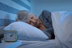 灰白头发的老太太晚上睡得很安稳。躺在家里睡觉的高级女人。成熟的女人在晚上睡觉的时候感到轻松自在.