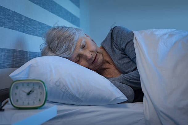 灰白头发的老太太晚上睡得很安稳。躺在家里睡觉的高级女人。成熟的女人在晚上睡觉的时候感到轻松<strong>自在</strong>.