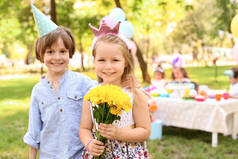 小女孩与花和可爱的男孩在户外生日聚会上