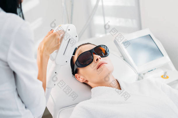 妇女在防护眼镜获得激光脱毛美容师在温泉沙龙