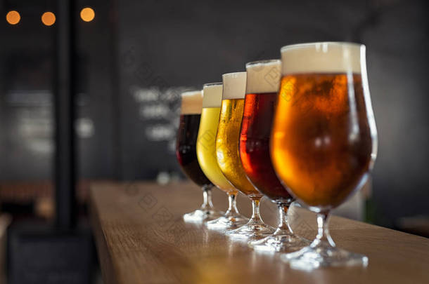 在木制酒吧用不同种类的工艺啤酒的眼镜。在一排的酒杯里轻拍啤酒。五杯不同类型的啤酒在酒吧特写.