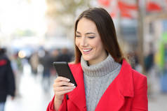 快乐的妇女在红色检查电话信息在街道在冬天