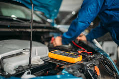 带万用表的汽车电工检查电池电量。自动服务、车辆布线诊断