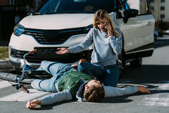 女子拨打紧急电话, 看着交通碰撞后躺在路上的受伤骑自行车的人 