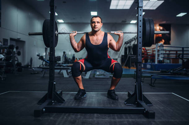 肌肉力量提升者在健身房里和杠铃一起做蹲。举重锻炼, 举重训练, 运动俱乐部的举重运动员
