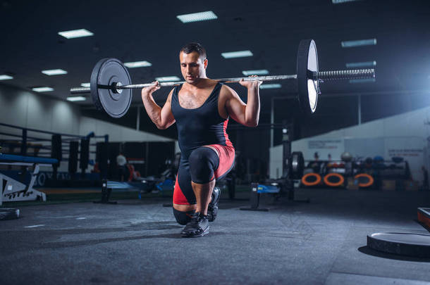 强大的举重运动员在健身房里用杠铃做蹲, 负重。健身俱乐部举重锻炼, 健美训练