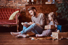 爱, 家庭, 父爱, 圣诞节。英俊的父亲读他的女儿童话故事, 而他们坐在地板上周围的礼物