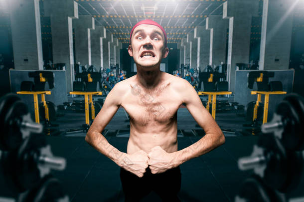 瘦家伙在健身房锻炼时摆姿势, 瘦身营养不良显示肌肉在体育俱乐部, 有趣的健美运动员