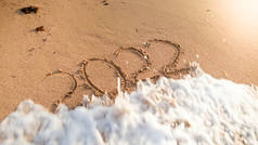 在岛屿海滩上的湿沙上写着的海浪滚动超过2022年新年数字的特写镜头照片。新年、圣诞节和寒假旅行的概念.