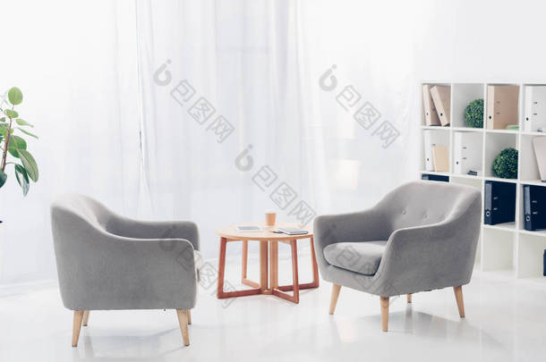 内部的轻现代<strong>商务办公室</strong>与两个扶手椅, 架子, 植物和小木桌上的薄纱背景