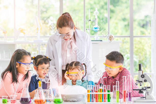 科学老师在实验室教亚洲学生, 烟从碗里飘出来, 他们兴奋, 五颜六色的试管和显微镜放在实验室的桌子上, 在实验室学习的概念.
