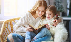 幸福的家庭母亲在冬天早上给孩子读书给女儿看窗户