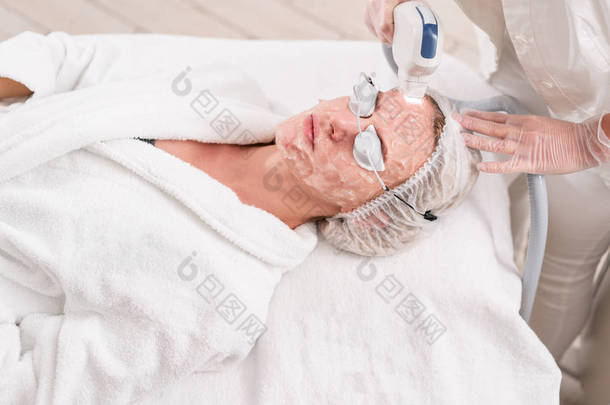 用专业设备进行抗痤疮光疗。美丽的女人在美容院在照片恢复过程中。在美容诊所进行激光面部皮肤治疗。硬件美容