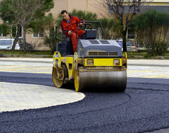 工人们领着震动的公路滚子把铺好的柏油压紧，以便铺筑公路