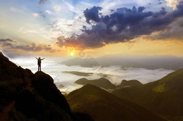 宽广的山全景。小剪影的游客与背包在洛基山坡上举起手在山谷覆盖着白色的肿胀云。自然美、旅游观与旅游理念