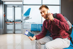 微笑的人说话的智能手机, 而坐在机场与背包