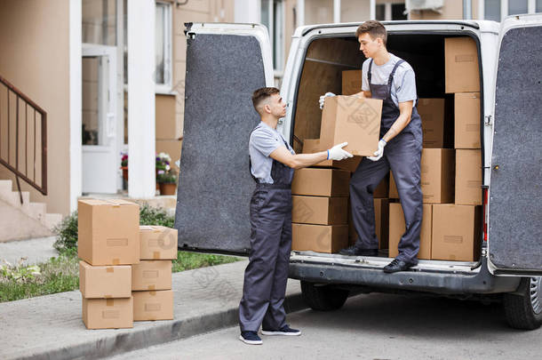 两个穿着制服的年轻帅哥正在卸货的面包车装满箱子。房子移动, 搬运工服务