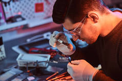 电子技术人员用放大镜仔细修补破损的平板电脑, 仔细检查平板电脑的芯片。红色和蓝色灯光照明