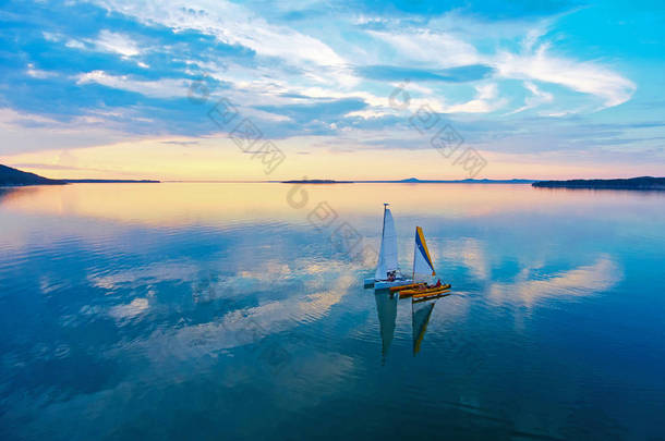 日落时在伊曼陶湖上航行的双体船。从上面看。风景如画的日落。云反射在水中。哈萨克斯坦伊曼陶湖.
