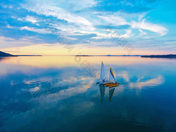 日落时在伊曼陶湖上航行的双体船。从上面看。风景如画的日落。云反射在水中。哈萨克斯坦伊曼陶湖.