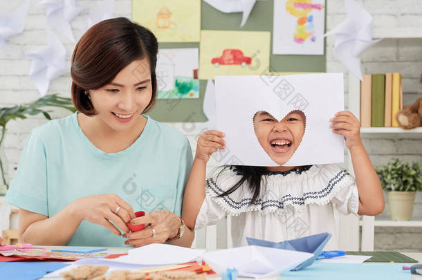 小亚洲女孩坐在老师和乐趣与剪纸在艺术课上切出心