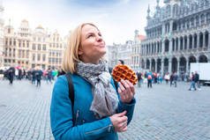 年轻的漂亮女人拿着传统的比利时华夫饼在比利时布鲁塞尔大市场广场的背景
