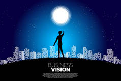 商人的剪影指向月亮在城市的夜晚。成长型企业理念，事业成功之路.