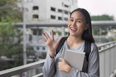 愉快微笑的亚洲女大学生的肖像指着5个手指, 5 分姿势;城市校园环境中的第五理念