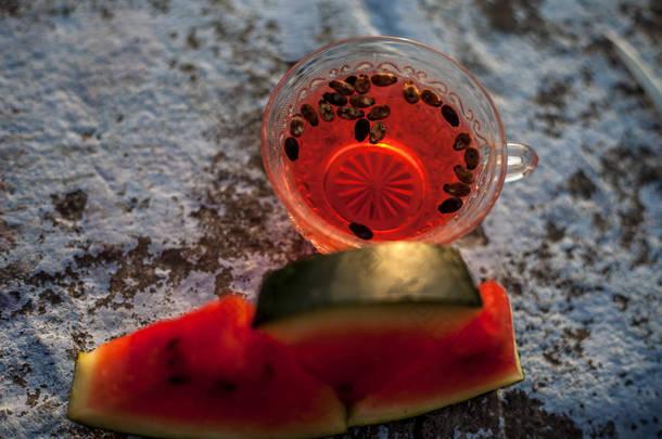 西瓜种子茶在一个透明的玻璃杯在粗糙的表面与一些种子和三角形切西瓜片。热门镜头.