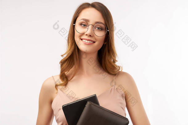 一个漂亮的年轻女学生迷人地微笑着，手里拿着笔记本。长长的卷曲的黑发和大圆眼镜