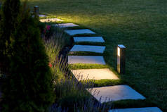 在后院花园中，一盏灯笼照亮了方形瓷砖的大理石小径，在后院花园中，有花坛和草坪复制空间。.