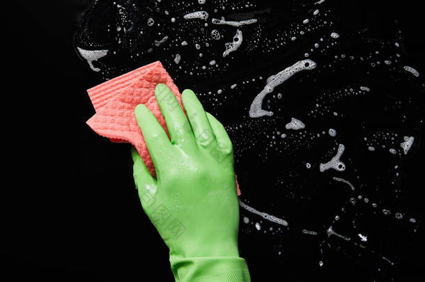 裁剪视图的人在橡胶手套清洁与粉红色抹布在黑色背景 