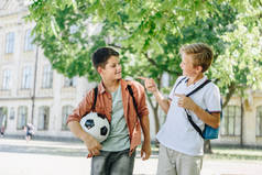 两个带着背包的快乐小学生在绿色公园里散步时说话 